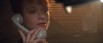 Movie still from “The Adventures of Ford Fairlane” (1990), directed by Renny Harlin – A young woman talking on a phone in a dimly - lit room; Close Up shot, Low angle
