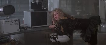 Movie still from “The Adventures of Ford Fairlane” (1990), directed by Renny Harlin – A woman sitting on a chair in front of a computer monitor; Medium shot, Low angle