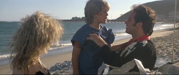 Movie still from “The Adventures of Ford Fairlane” (1990), directed by Renny Harlin – A young woman is talking to an older man on the beach; Medium shot, Over the shoulder angle