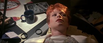 Movie still from “The Adventures of Ford Fairlane” (1990), directed by Renny Harlin – A woman with red hair laying on top of a table; Close Up shot, High angle