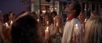 Movie still from “The Adventures of Ford Fairlane” (1990), directed by Renny Harlin – A group of people holding lit candles in a room; Medium shot, Low angle