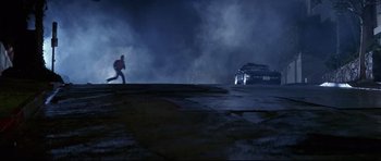 Movie still from “The Adventures of Ford Fairlane” (1990), directed by Renny Harlin – A man running in the dark near a car on the road; Wide shot, High angle