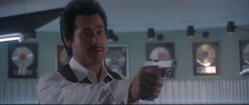 Movie still from “The Adventures of Ford Fairlane” (1990), directed by Renny Harlin – A man holding a gun while wearing a suit; Close Up shot, Low angle