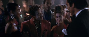 Movie still from “The Adventures of Ford Fairlane” (1990), directed by Renny Harlin – A man and a woman posing for a picture in front of a crowd; Close Up shot, Over the shoulder angle