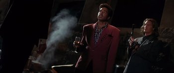 Movie still from “The Adventures of Ford Fairlane” (1990), directed by Renny Harlin – A man holding a wine glass and smoking a cigarette; Medium shot, Low angle