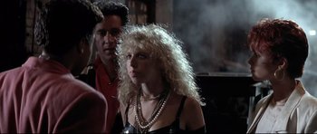 Movie still from “The Adventures of Ford Fairlane” (1990), directed by Renny Harlin – A woman with blonde curly hair wearing a black dress; Medium shot, Over the shoulder angle