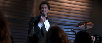 Movie still from “The Adventures of Ford Fairlane” (1990), directed by Renny Harlin – A man in a tuxedo is speaking into a microphone; Medium shot, Low angle