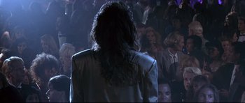 Movie still from “The Adventures of Ford Fairlane” (1990), directed by Renny Harlin – A woman standing in front of a crowd of onlookers; Medium shot, Over the shoulder angle