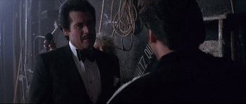 Movie still from “The Adventures of Ford Fairlane” (1990), directed by Renny Harlin – A man in a tuxedo talking to another man in a suit; Medium shot, Over the shoulder angle