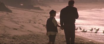 Movie still from “The Adventures of Ford Fairlane” (1990), directed by Renny Harlin – A man and a woman holding hands on the beach; Medium shot, Over the shoulder angle