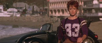Movie still from “The Adventures of Ford Fairlane” (1990), directed by Renny Harlin – A woman standing in front of a black car; Medium shot, Low angle