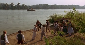 Movie still from “The Adventures of Huck Finn” (1993), directed by Stephen Sommers – A group of people standing on top of a sandy beach next to a body of water; Extreme Wide shot, High angle