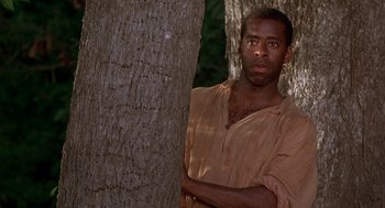 Movie still from “The Adventures of Huck Finn” (1993), directed by Stephen Sommers – A man standing next to a tree with his arms crossed; Medium shot, Over the shoulder angle
