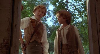Movie still from “The Adventures of Huck Finn” (1993), directed by Stephen Sommers – Two young men in old - fashioned clothing standing next to each other in a wooded area; Medium shot, Low angle