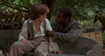 Movie still from “The Adventures of Huck Finn” (1993), directed by Stephen Sommers – Two people sitting on a park bench one of which is holding a tie; Medium shot, Over the shoulder angle
