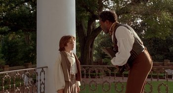 Movie still from “The Adventures of Huck Finn” (1993), directed by Stephen Sommers – A young boy and an older man talking on a porch; Medium shot, Over the shoulder angle