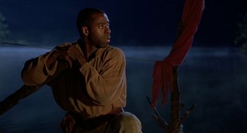 Movie still from “The Adventures of Huck Finn” (1993), directed by Stephen Sommers – A man sitting on top of a tree at night; Medium shot, Low angle
