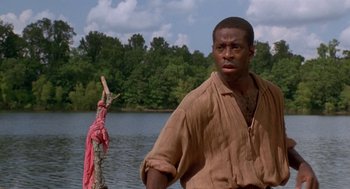 Movie still from “The Adventures of Huck Finn” (1993), directed by Stephen Sommers – A man standing in front of a body of water; Medium shot, Low angle
