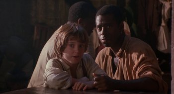 Movie still from “The Adventures of Huck Finn” (1993), directed by Stephen Sommers – A boy and a man sitting at a wooden table; Medium shot, Over the shoulder angle