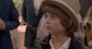 Movie still from “The Adventures of Huck Finn” (1993), directed by Stephen Sommers – A young boy wearing a hat looking to his left; Close Up shot, Over the shoulder angle