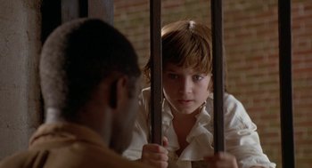 Movie still from “The Adventures of Huck Finn” (1993), directed by Stephen Sommers – A young girl looking at a man through bars; Close Up shot, Over the shoulder angle