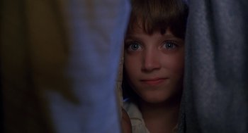 Movie still from “The Adventures of Huck Finn” (1993), directed by Stephen Sommers – A young girl is peeking out from behind a curtain; Close Up shot, Over the shoulder angle