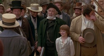 Movie still from “The Adventures of Huck Finn” (1993), directed by Stephen Sommers – An old man and a young boy are standing in front of a group of people; Medium shot, Over the shoulder angle
