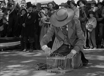 Movie still from “The Adventures of Mark Twain” (1944), directed by Irving Rapper – A man in a hat is sitting on the ground with a bird cage; Medium shot, Low angle