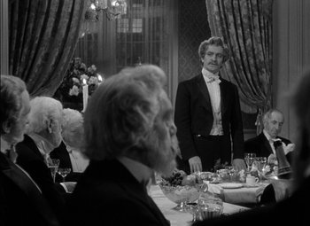 Movie still from “The Adventures of Mark Twain” (1944), directed by Irving Rapper – A man in a tuxedo standing in front of a group of diners; Medium shot, Over the shoulder angle