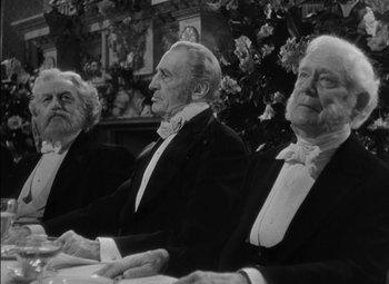 Movie still from “The Adventures of Mark Twain” (1944), directed by Irving Rapper – A group of men sitting next to each other in tuxedos; Medium shot, Over the shoulder angle