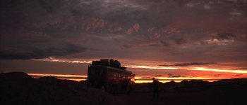 A man standing in front of a bus on a dirt road