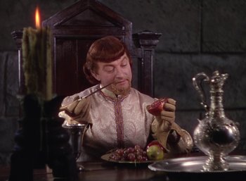 Movie still from “The Adventures of Robin Hood” (1938), directed by William Keighley – A woman sitting at a table with a plate of food; Medium shot, High angle