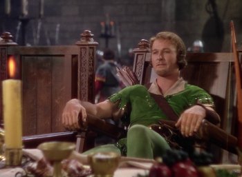 Movie still from “The Adventures of Robin Hood” (1938), directed by William Keighley – A man sitting in a chair in front of a table with food on it; Medium shot, High angle