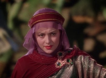 Movie still from “The Adventures of Robin Hood” (1938), directed by William Keighley – A woman in a red and purple dress and a purple headscarf; Close Up shot, Over the shoulder angle