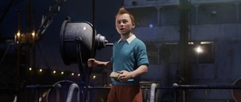 Movie still from “The Adventures of Tintin” (2011), directed by Steven Spielberg – A young boy holding a piece of paper in front of a machine; Medium shot, High angle