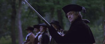Movie still from “The Affair of the Necklace” (2001), directed by Charles Shyer – A man holding a rifle in front of a crowd; Medium shot, Low angle