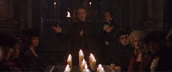 Movie still from “The Affair of the Necklace” (2001), directed by Charles Shyer – A man standing in front of a group of lit candles; Medium shot, Over the shoulder angle