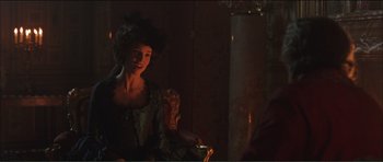 Movie still from “The Affair of the Necklace” (2001), directed by Charles Shyer – A woman sitting in a chair in a dark room; Medium shot, Over the shoulder angle