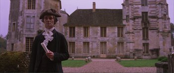 Movie still from “The Affair of the Necklace” (2001), directed by Charles Shyer – A man wearing a hat standing in front of a building; Medium shot, Low angle