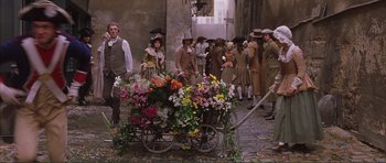 Movie still from “The Affair of the Necklace” (2001), directed by Charles Shyer – A group of people standing next to a cart filled with flowers; Wide shot, High angle
