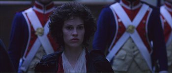 Movie still from “The Affair of the Necklace” (2001), directed by Charles Shyer – A woman with curly black hair standing in front of a wall; Close Up shot, Over the shoulder angle