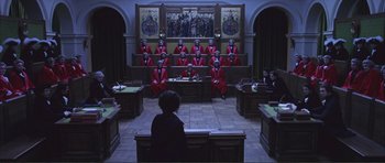 Movie still from “The Affair of the Necklace” (2001), directed by Charles Shyer – A group of men in red suits sitting in front of a judge; Extreme Wide shot, High angle