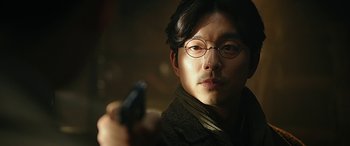A man with glasses holding a gun in his hand