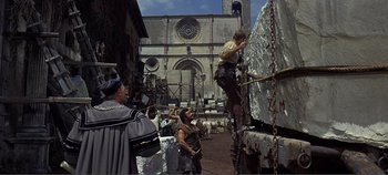 Movie still from “The Agony and the Ecstasy” (1965), directed by Carol Reed – A group of people standing on top of a truck in front of a building; Wide shot, Over the shoulder angle