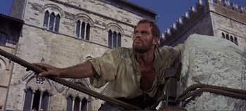 Movie still from “The Agony and the Ecstasy” (1965), directed by Carol Reed – A man with a beard is standing in front of an old building; Medium shot, Low angle