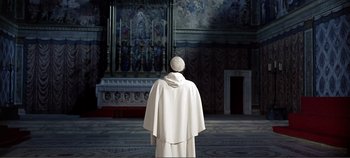 Movie still from “The Agony and the Ecstasy” (1965), directed by Carol Reed – A man in a white robe and a white hat stands in front of a painting; Wide shot, High angle