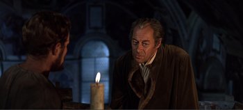 An older man in a fur coat looking at a lit candle