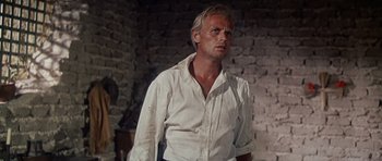 Movie still from “The Alamo” (1960), directed by John Wayne – A man wearing a white shirt standing next to a brick wall; Medium shot, Low angle