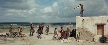 Movie still from “The Alamo” (1960), directed by John Wayne – A group of people riding horses in a dirt field; Extreme Wide shot, Low angle