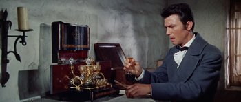 Movie still from “The Alamo” (1960), directed by John Wayne – A man sitting at a table holding a glass of red wine; Medium shot, Low angle
